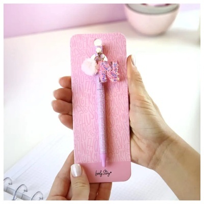 Caneta cor-de-rosa com pendentes na mão em cartão cor-de-rosa com padrão de letras