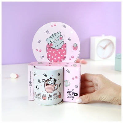 Caneca de cerâmica branca decorada com gatos e motivos rosa, em caixa rosa com desenho de gato, sobre superfície branca.