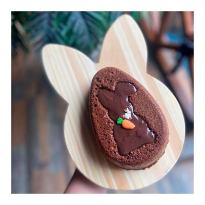 Bolo de chocolate em forma oval com decoração de coelho e cenoura em base de madeira em forma de cabeça de coelho.