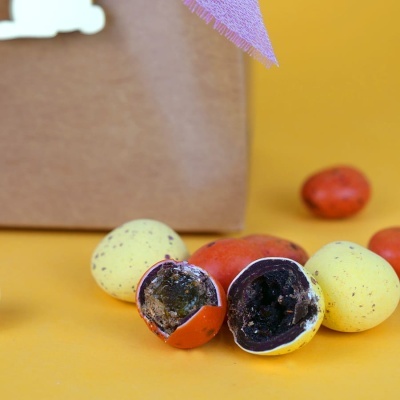 Ovos de Páscoa de chocolate amarelos e vermelhos partidos mostram interior de chocolate sobre superfície amarela.