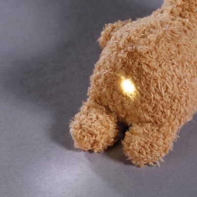 Brinquedo peluche castanho claro com luz amarela na pelagem sobre superfície cinza