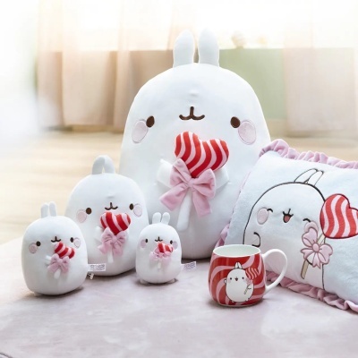 Peluches de coelho brancos com corações vermelhos, almofada e caneca decorados num ambiente claro