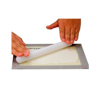 Mãos usando rolo de massa branco sobre tapete com régua