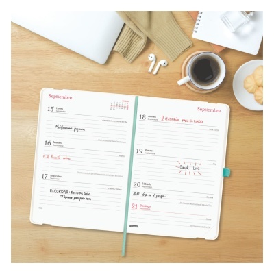 Agenda aberta em duas páginas na mesa com notas manuscritas, AirPods, caneca de café e caderno