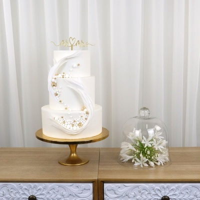 Bolo de casamento branco decorado com bolinhas e penas e flores brancas sob campânula de vidro