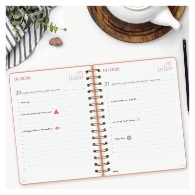 Agenda semanal aberta com espiral dourado sobre mesa com toalha, xícara branca e lápis preto