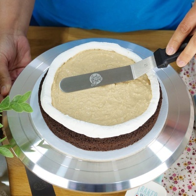 Bolo de chocolate com cobertura creme colocado num prato metálico com espátula de metal e cabo preto