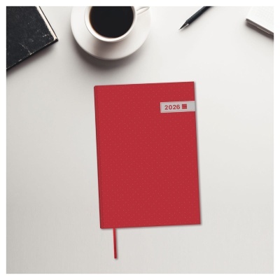 Agenda vermelha 2026 com marcador sobre mesa branca com caneca de café e caneta.