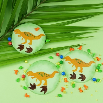 Bolachas decoradas com dinossauros e confeitos coloridos sobre fundo verde