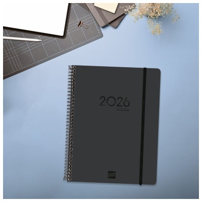 Caderno preto com espiral e número 2026 impresso na capa sobre uma superfície azul.