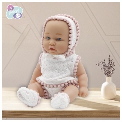 Boneca de bebé vestida de branco e rosa sentada em madeira com vaso ao lado.