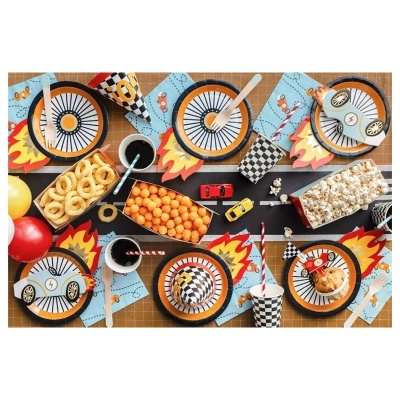 Mesa de festa com decoração temática de carros, pratos e copos de papel, snacks e brinquedos coloridos.