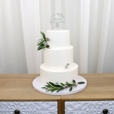 Bolo de três andares branco com folhas verdes e bolas prateadas, topo com texto Nosso Batismo