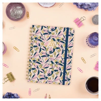 Caderno espiral com padrão floral e número 26, rodeado por artigos de escritório