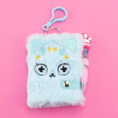 Caderneta peluda azul clara com olhos bordados, fecho de botão e caneta rosa ao lado com decoração vermelha.