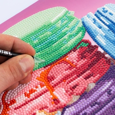 Mão a colocar pequenas pedras coloridas num desenho em papel com padrão colorido.