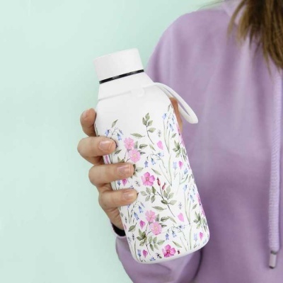 Garrafa de água branca com padrão floral segurada por pessoa com roupa lilás