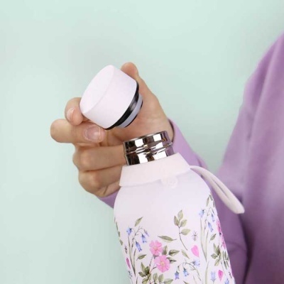 Garrafa térmica branca com flores coloridas e tampa branca sendo segurada por uma mão