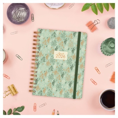 Agenda 2026 verde com folhas, espiral dourada e elástico verde, em superfície rosa com material de escritório