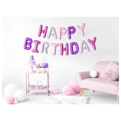 Decoração de aniversário com balões HAPPY BIRTHDAY em rosa, roxo e branco num espaço com carrinho de bolos e sofá cor de rosa.