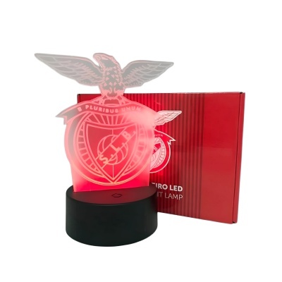 Lâmpada LED em forma de escudo e águia iluminada em vermelho com embalagem vermelha ao fundo.