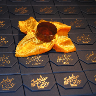 Caixas azuis octogonais com texto dourado e jarra metálica sobre tecido de veludo dourado