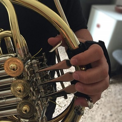 Trompa dourada com botões detalhados e mão com anel e proteção preta