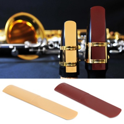 Bocal dourado com detalhes em preto e vermelho com duas palhetas bege e castanho sobre fundo com instrumentos de metal desfocados