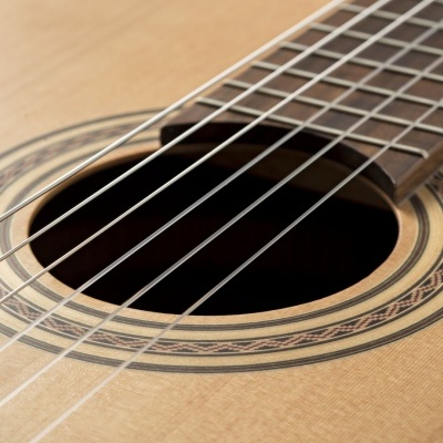 Violão acústico em madeira clara com cordas e padrão circular ao redor da boca