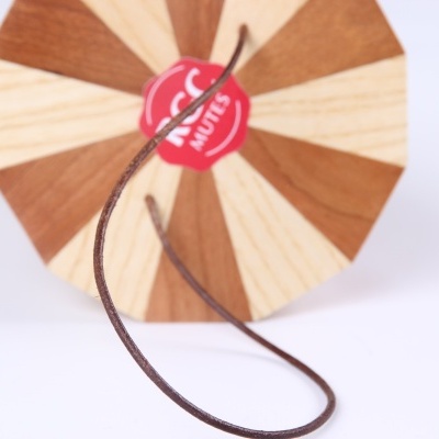 Objeto decorativo redondo com padrão castanho e bege e etiqueta vermelha com texto MUTE