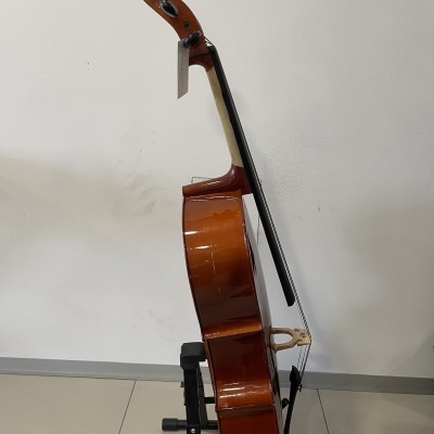 Violoncelo castanho em suporte negro contra parede branca