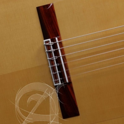 Close-up do tampo de uma guitarra acústica com ponte em madeira escura e cordas de nylon.