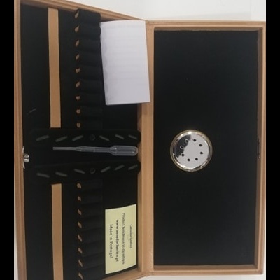 Estojo de madeira aberto com interior preto, ferramenta metálica e etiquetas visíveis.