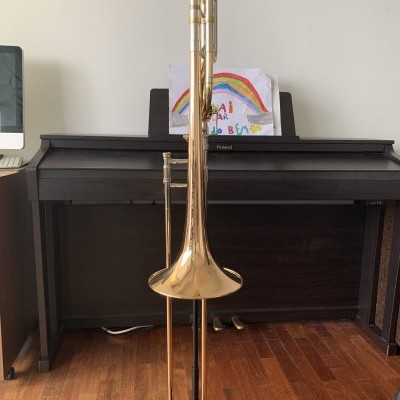 Trombone dourado em suporte diante de piano digital preto com desenho infantil colorido no suporte de partitura