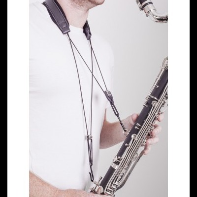 Pessoa com t-shirt branca segura saxofone negro com correia preta de couro
