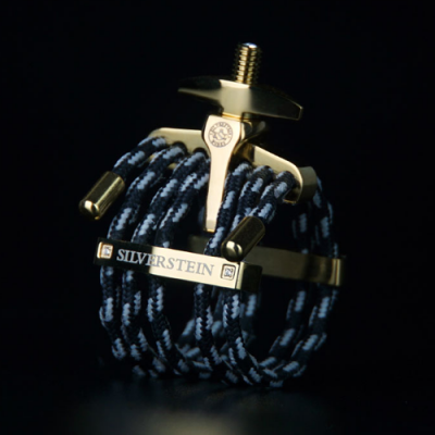 Abraçadeira metálica dourada com corda preta e branca, marca SILVERSTEIN visível