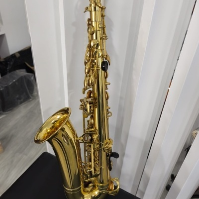 Saxofone tenor dourado em superfície preta com fundo branco e chão cinzento