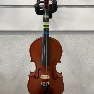 Violino de madeira castanha com etiquetas coloridas no braço, pendurado numa parede branca