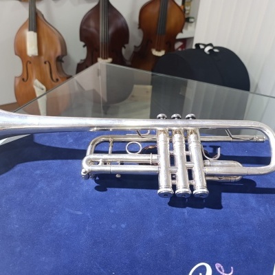 Trompete prateado sobre pano azul com contrabaixos ao fundo