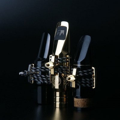 Três bocaletes para saxofone em preto e dourado, com ligaduras e abraçadeiras sobre fundo escuro.