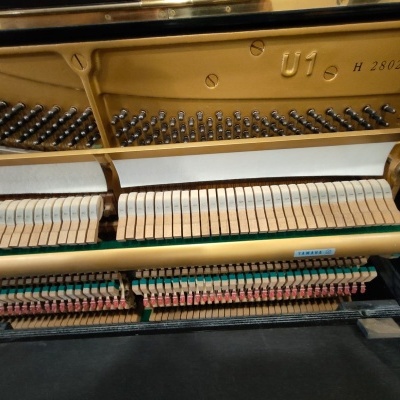 Mecanismo interno de piano vertical Yamaha com martelos de madeira e estrutura metálica dourada.