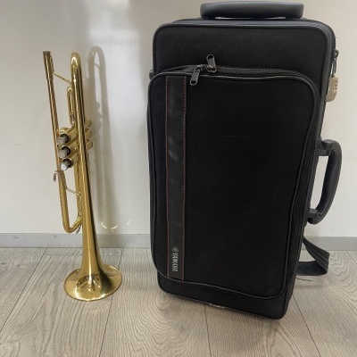 Trompete dourado e estojo preto para instrumento em ambiente com chão de madeira clara