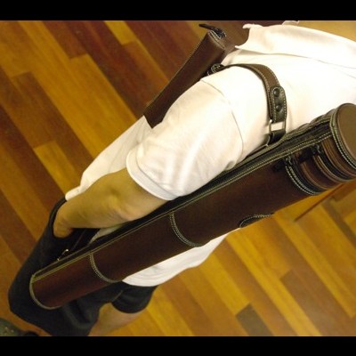 Pessoa com estojo cilindrico castanho em couro nas costas, chão de madeira clara