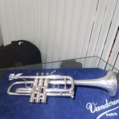 Trompete prateado sobre pano azul Vandoren PARIS em mesa de vidro