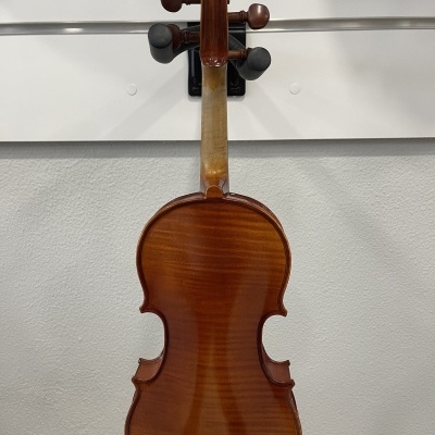 Violino em madeira castanha pendurado de costas numa parede cinza
