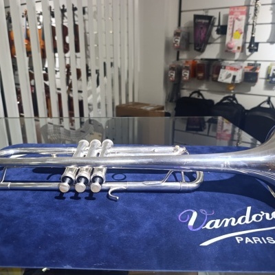Trompete prateado sobre pano azul com texto Vandoren Paris em loja de música