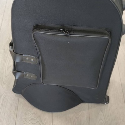 Mala preta arredondada com bolso frontal e alças laterais em chão de madeira