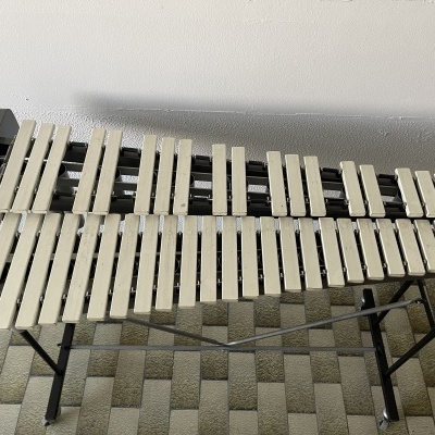 Xilofone com teclas brancas em suporte preto, chão colorido e parede branca