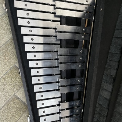 Xilofone metálico com estojo preto aberto em chão de ladrilhos