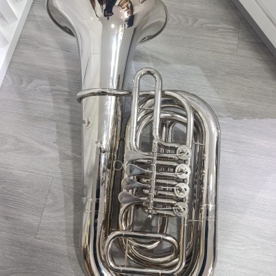 Tuba de metal prateado com pistões sobre chão cinzento de madeira